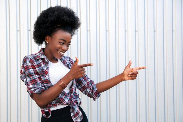 Koncepcja promocji. Radosna Afroamerykanka, wskazująca na wolną przestrzeń, polecająca coś. Szare tło. - Zdjęcie, obraz