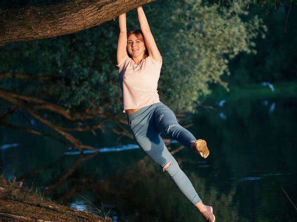 Menina bonita se divertindo na natureza junto ao rio. Balançando em um galho de árvore
 - Foto, Imagem