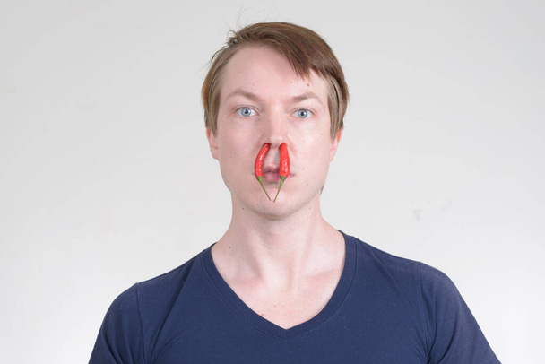 Portrait of young handsome man with chili peppers inside nose - Foto, Imagem