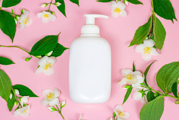 コピースペース付きピンクの背景に鮮やかな新鮮なジャスミンの花とモックアップとしてクリームを保湿するための白いプラスチック化粧品容器のトップビュー。ボディ&スキンケア&ビューティーコンセプト. - 写真・画像