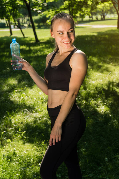 Beautiful girl holds a shaker with water. concept of fitness trainer holds a bottle for the time that he trained - Foto, Bild