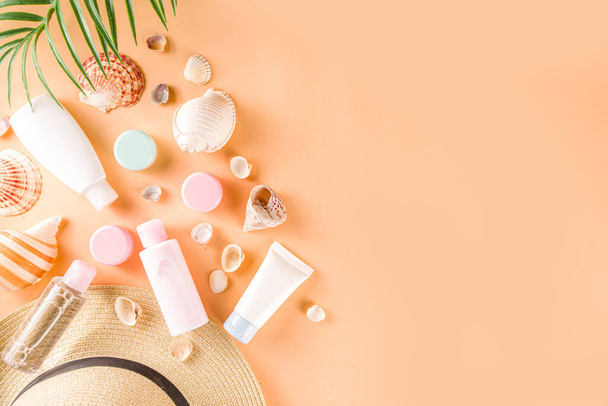 Summer cosmetics background. Summer skincare, sunscreen cosmetics, travel kit miniatures flat lay. Trendy peach background, with women bag, sea shells, tropical leaves, straw hat. Copy space above  - Photo, Image