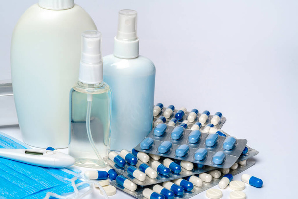 bottle of sanitizer or liquid soap, protective mask, medicine pills blisters and thermometer over light grey background - Fotó, kép