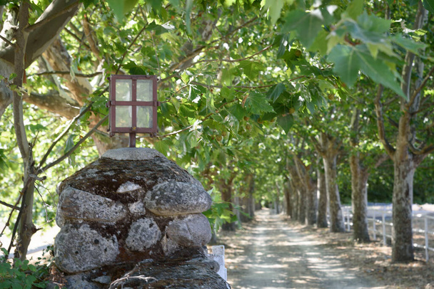 Palo in pietra con lanterna di ferro all'ingresso di un sentiero alberato. Accesso ad una fattoria. - Foto, immagini