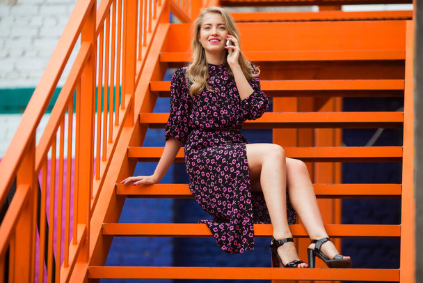  beautiful young woman in a dress near a bright orange staircase with a phone - Foto, Bild