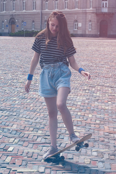 Teen girl performs a skateboard stunt on a warm summer day in the center of European city - Фото, зображення