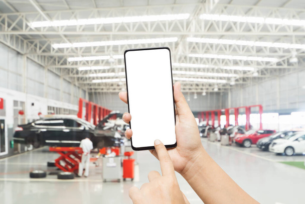 Mock up smartphone for automobile online service mobile application. Mockup blank white screen mobile phone with finger point and touch on touchsreen in  Auto repair shop. - Photo, Image