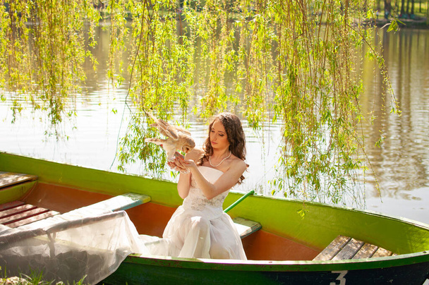 Magic portrait of beautiful bride in white wedding dress with real barn owl on boat - Photo, image