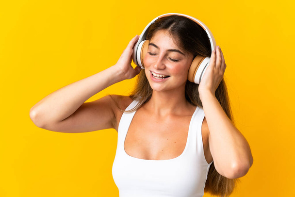 Sarı arka planda izole edilmiş genç beyaz kadın müzik dinliyor. - Fotoğraf, Görsel
