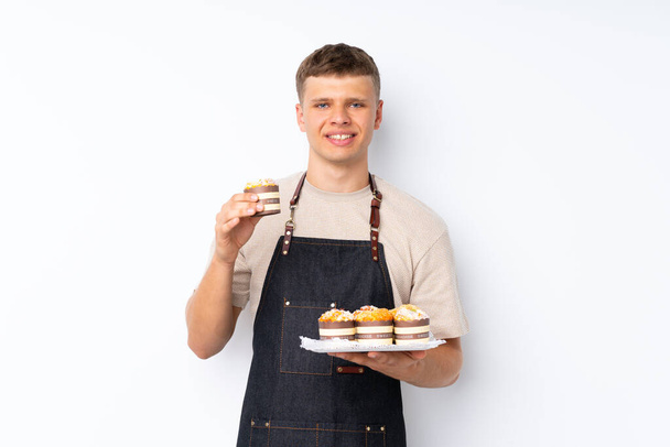 Young handsome man over isolated white background holding mini cakes - Photo, Image