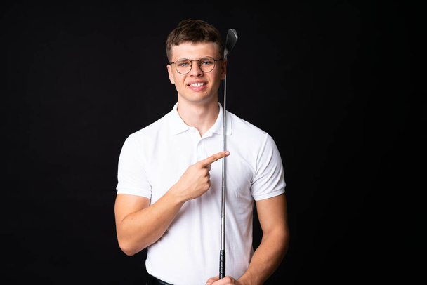 Handsome young golfer player man over isolated black background - Fotoğraf, Görsel