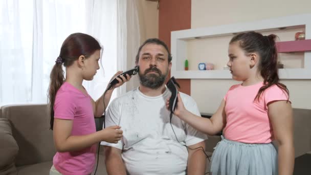 Dos niñas recortan la barba de su padre con cortadoras eléctricas durante la cuarentena. Adaptación a la distancia social. Concepto de aislamiento social
. - Imágenes, Vídeo
