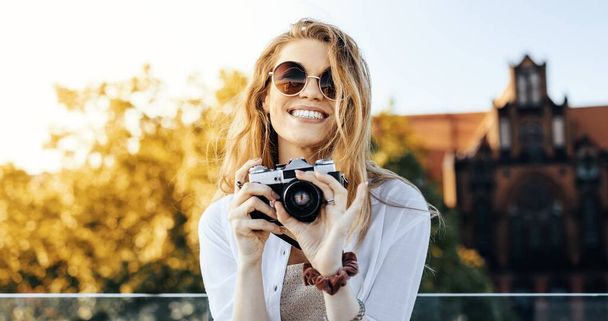 A close up shot of a smiling, fashionably dressed blonde woman posing with a camera - Foto, immagini