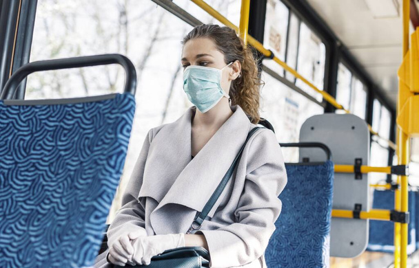 A young female wearing a facemask and sitting in a bus under the sunlight - COVID-19 - 写真・画像