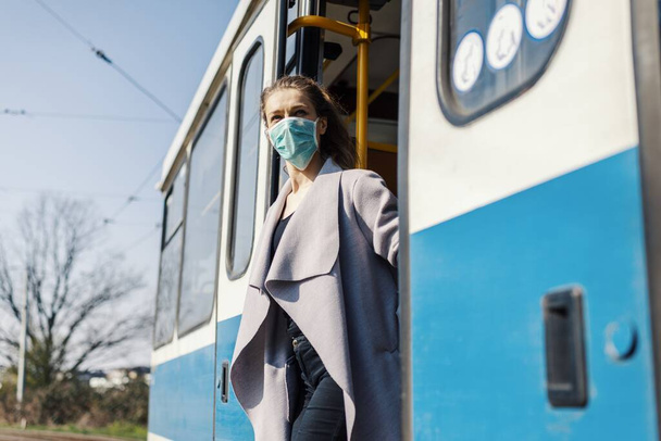 A young female wearing a facemask and gloves getting off a bus under the sunlight - COVID-19 - Foto, Bild
