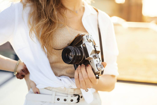 A close up shot of a happy, fashionably dressed female traveler with camera on a sunny weather - Zdjęcie, obraz