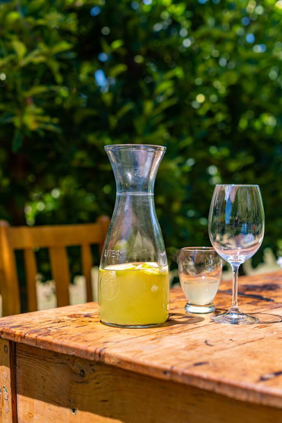 A vertical image of a jar of juice with drinking glasses on a wooden table set outdoors - Zdjęcie, obraz