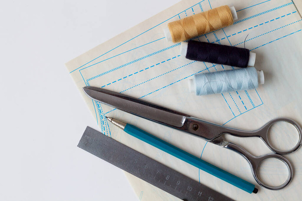 nici do szycia, ołówki, linijka, nożyczki i wzory na białym stole projektanta mody. Widok z góry. skopiować przestrzeń. narzędzia biurowe - Zdjęcie, obraz