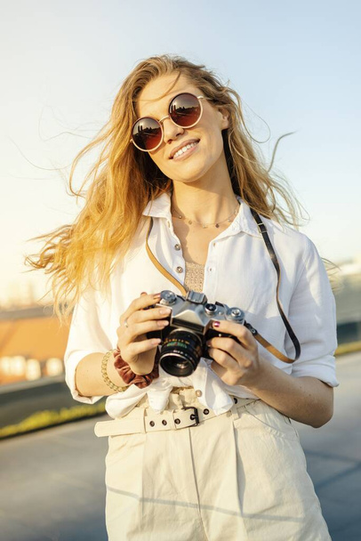 A vertical shot of a happy, fashionably dressed female traveler with camera on a sunny weather - Foto, immagini