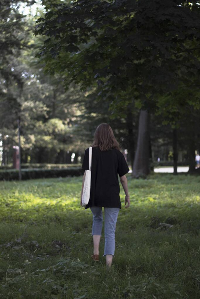 A vertical shot of a female with a white-colored tote bag while walking in a park - Photo, Image