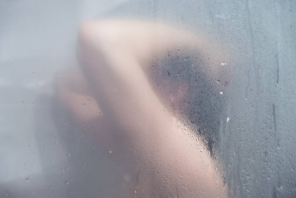 A female figure in a shower cabin behind wet glass - Foto, Imagen