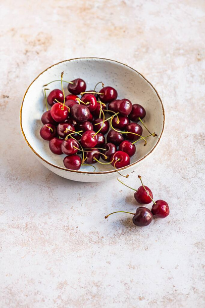 A vertical image of red ripe cherries in a bowl on a concrete surface - Foto, Bild
