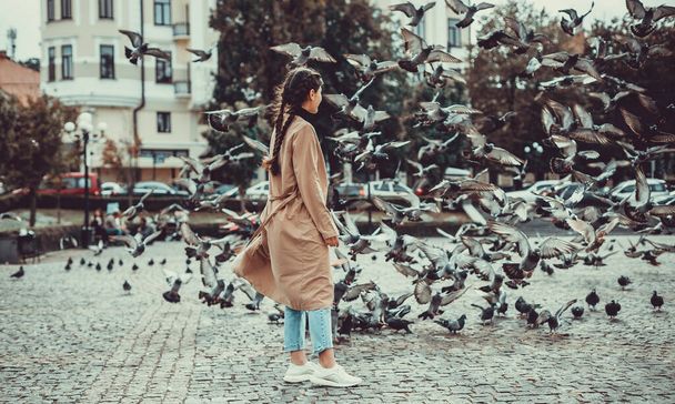 Back view of a girl, surrounded by flying doves on city background. - Fotografie, Obrázek
