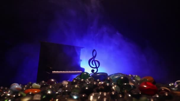Musikkonzept. Musikalisches Symbol Notenschlüssel aus Edelstahl Miniatur mit farbig getöntem Licht auf nebligem Hintergrund. Musikinstrumente im Schein der Dunkelheit. Selektiver Fokus - Filmmaterial, Video