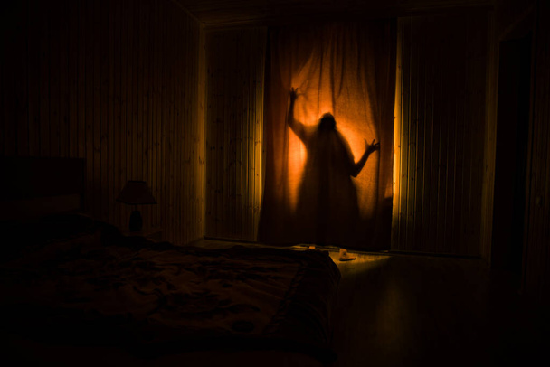 Horror silhouette in window with curtain inside bedroom at night. Horror scene. Halloween concept. Blurred silhouette of ghost - Φωτογραφία, εικόνα