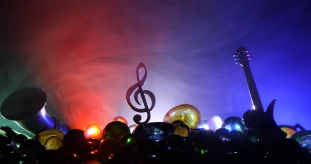 Muziekconcept. Muzikaal symbool treble clef RVS miniatuur met kleurrijk getint licht op mistige achtergrond. Muziekinstrumenten bij weinig licht. Selectieve focus - Video