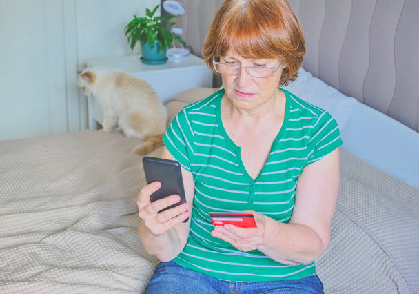 Femme âgée utilisant un téléphone dans sa chambre à la maison. Joyeux retraité faisant du shopping en ligne sur le lit. Mode de vie. Espace de copie - Photo, image