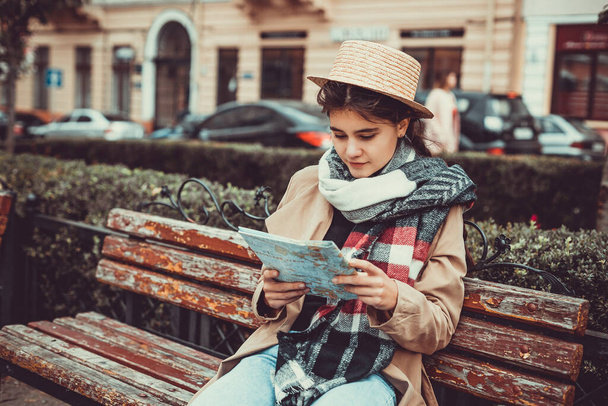 Lovely tourist got lost in a foreign city and looks at a map to find way out while sitting on a bench. - Foto, Bild