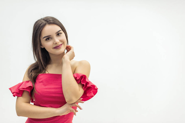 Attractive beautiful girl in a red dress with shoulders bare posing over white background. - Φωτογραφία, εικόνα