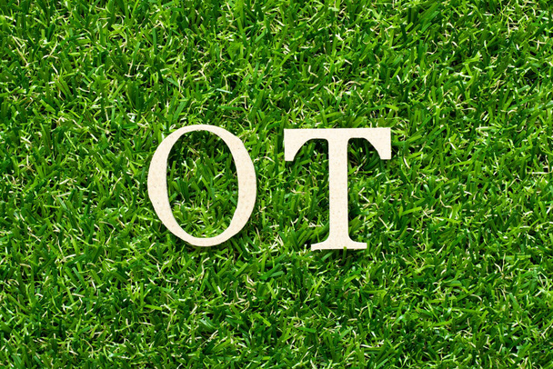 Alfabeto de madeira letra na palavra ot (abreviatura para horas extras) no fundo grama verde
 - Foto, Imagem