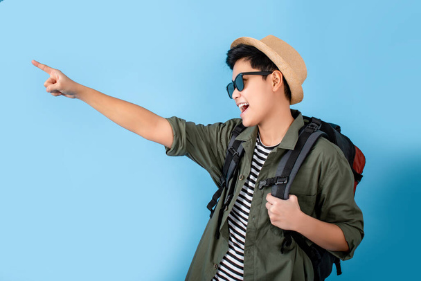Cheerful asian tourists. He pointed to an empty space on a blue background. - Photo, Image
