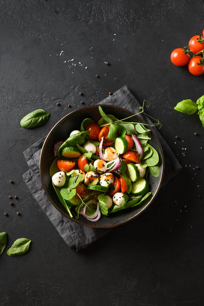 Salad with spinach, onion, cucumber, summer vegetables and Mozzarella on black background. Top view. Vertical format. - Foto, afbeelding