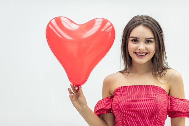 Усміхнена жінка стоїть на білому тлі з червоними кульками у формі серця в руках
. - Фото, зображення