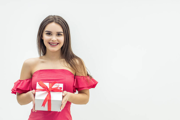 Joyful woman holding a gift box and smiling over a white background. - Fotografie, Obrázek