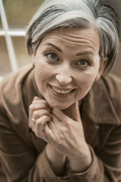 Happy mid aged woman toothy smiles looking at camera. Caucasian gray-haired model, close up portrait. Top view. Toned image - Zdjęcie, obraz