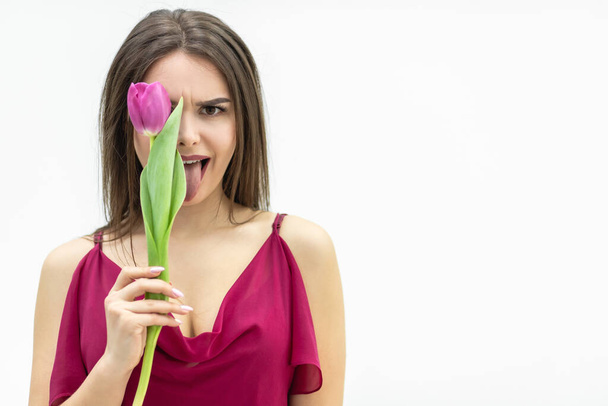 Cheerful lady fooling around hiding her eye behind a tulip flower and making silly faces. - Zdjęcie, obraz