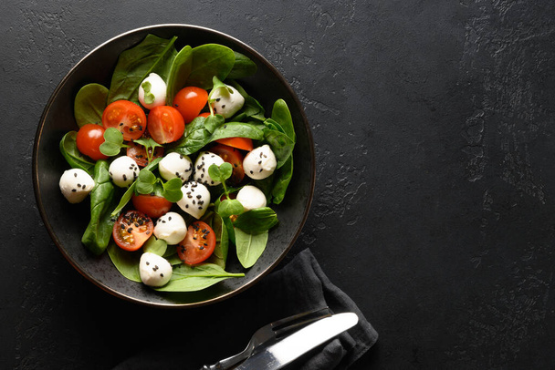 Summer salad with spinach, cherry tomatoes and Mozzarella cheese on black background. Copy space. - Foto, afbeelding