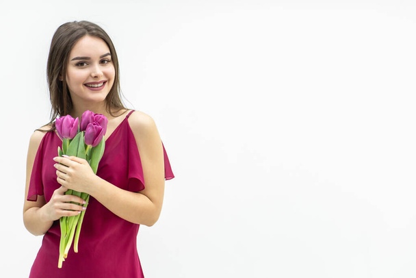 Cute girl with a bouquet of tulips looks with pleasure and smiles tenderly. - Φωτογραφία, εικόνα