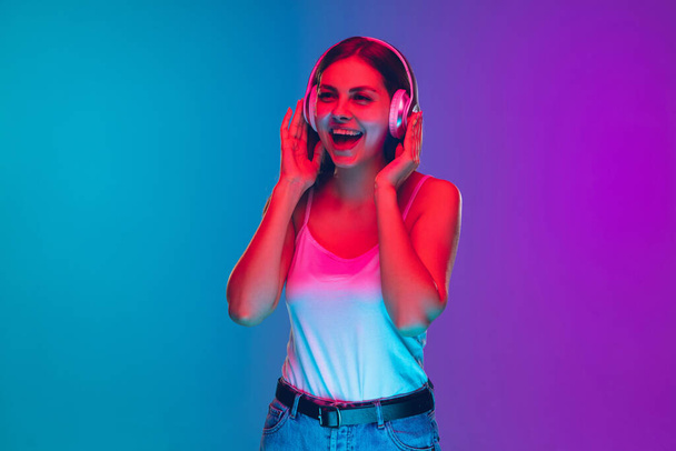 Caucasian young womans portrait isolated on gradient purple-blue background in neon light - Foto, immagini