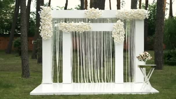 Luogo per la cerimonia di nozze in colore bianco. Arco da sposa quadrato bianco con mazzi di rose pastello nella foresta. - Filmati, video