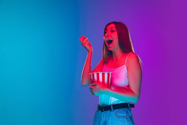 Caucasian young womans portrait isolated on gradient purple-blue background in neon light, cinema, movie watching - Zdjęcie, obraz