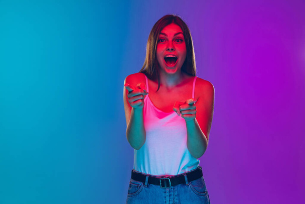Caucasian young womans portrait isolated on gradient purple-blue background in neon light, cinema, movie watching - Foto, immagini