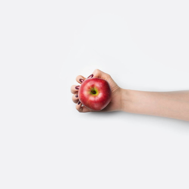 Female hand with red nails hold red apple on grey background - Valokuva, kuva