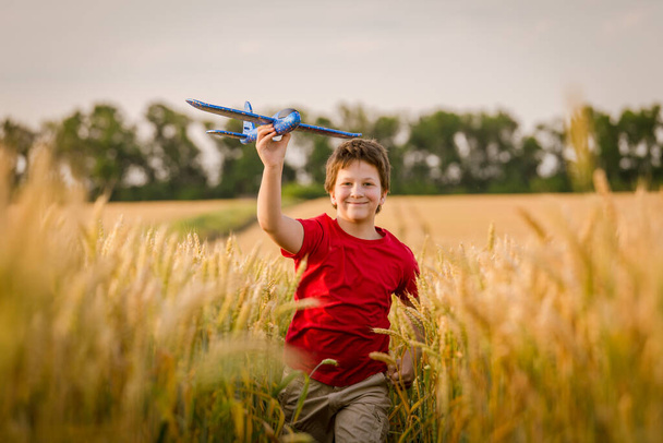 Boy running with toy plane on wheat field - Zdjęcie, obraz