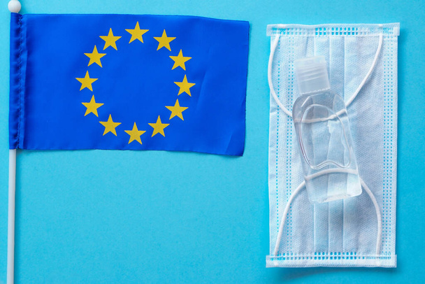 Medical, surgical mask and sanitizer or antibacterial soap, EU flag on blue background.Flatly with copy space. coronavirus preventive measure, top view. politics in europe, open borders - Photo, Image
