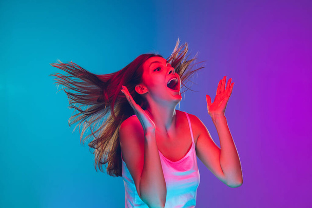 Caucasian young womans portrait isolated on gradient purple-blue background in neon light, cinema, movie watching - 写真・画像